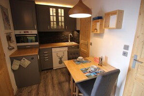 A compact kitchen with dark cabinets, a wooden countertop, a dishwasher, a coffee machine, and a dining table with a placemat.