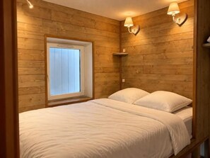 A wooden-paneled room with a bed, two wall-mounted lamps, and a window.