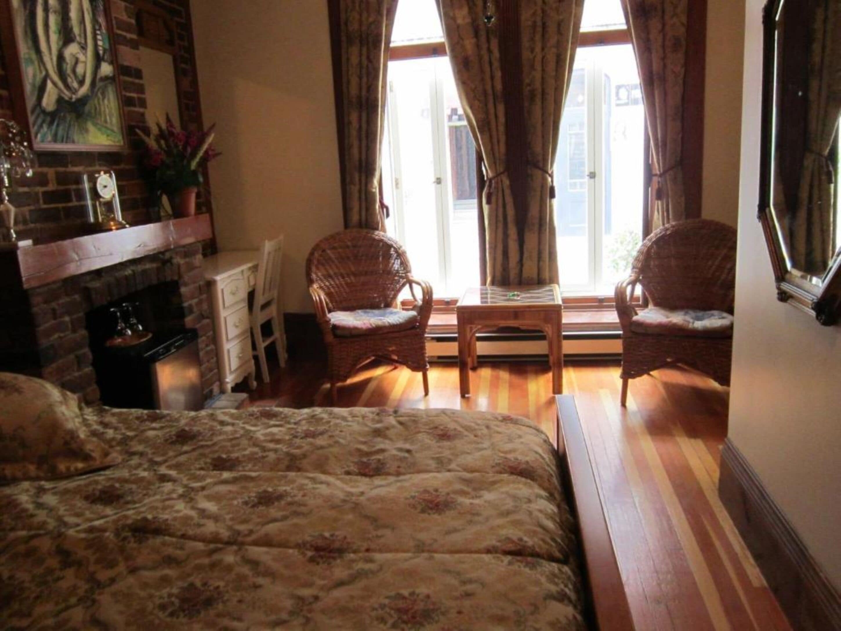 A cozy room with a bed, two wicker chairs, a small table, a fireplace, and a window with curtains.