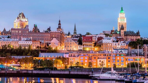 Bybillede med historiske bygninger, et markant tårn og en lystbådehavn med både.