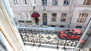 Udsigt fra en balkon over et gadebillede med en rød bil parkeret på fortovet.