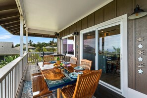 A covered outdoor dining area with a wooden table and chairs, a hammock, and a view of the surrounding neighborhood. - HALE LIO KAI: GORGEOUS HOME WITH POOL, HOT TUB & STUNNING OCEAN/SUNSET VIEWS (Kailua Kona)