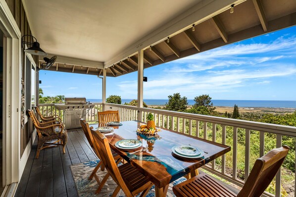 Un espacio de comedor al aire libre con vistas al océano, una parrilla y sillas de mimbre.
