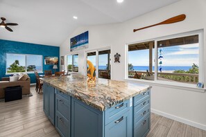 Una cocina moderna con una isla grande, muebles azules y vistas al océano.