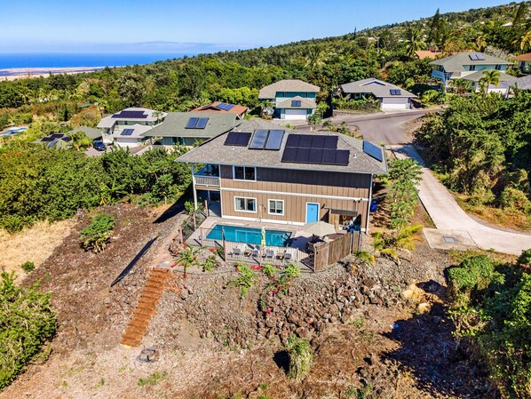A residential area with houses featuring solar panels, a swimming pool, and a rocky terrain. - HALE LIO KAI: GORGEOUS HOME WITH POOL, HOT TUB & STUNNING OCEAN/SUNSET VIEWS (Kailua Kona)