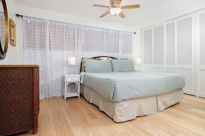 Une chambre à coucher comprenant un lit, des tables de chevet, un ventilateur de plafond et une armoire.
