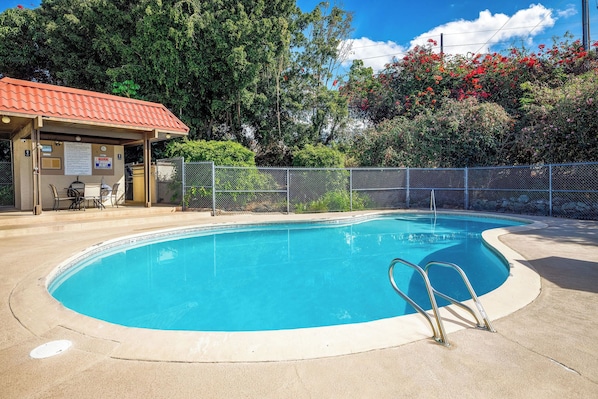 Une piscine d’un bleu éclatant, surveillée par un sauveteur posté sur une plateforme, entourée d’une clôture et agrémentée d’un espace de repos couvert avec un toit rouge.