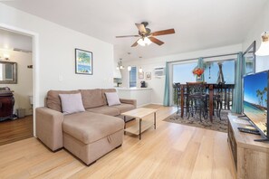 A modern living room with a sofa, coffee table, dining table with chairs, a ceiling fan, and a TV. - Kona Mansions#309 Top Floor,Beautiful, AC, Located in Heart of Town (Kailua Kona)