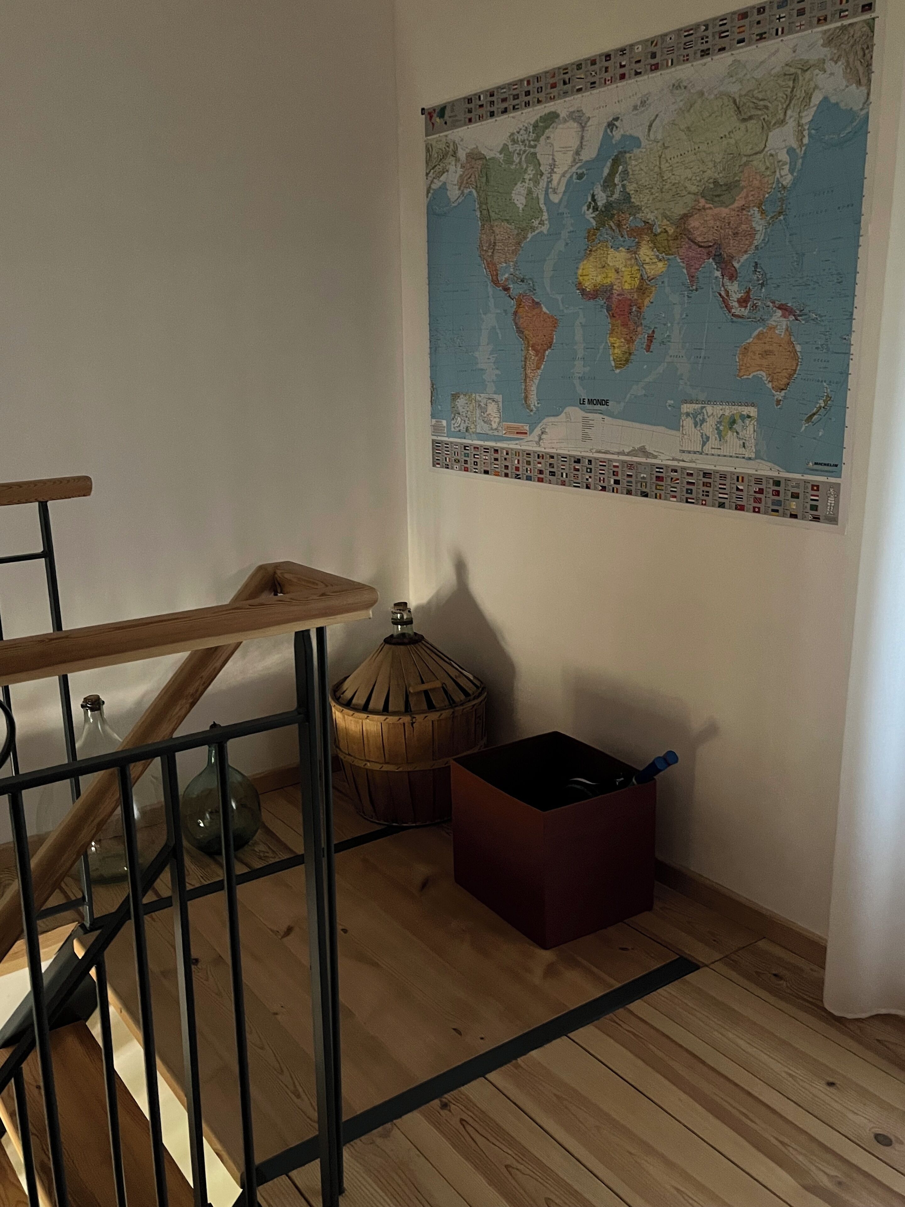 Een kamer met een houten trap, een wereldkaart aan de muur, een klein houten krukje en een rode opbergdoos.