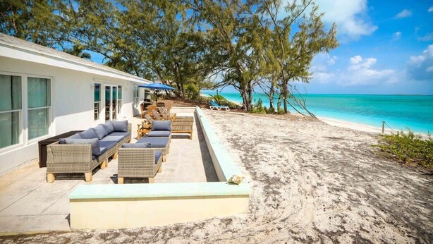 A beachfront property with a patio area featuring wicker furniture and a view of the ocean. - Beachfront White Palm Villa - Tar Bay (Rokers Point)