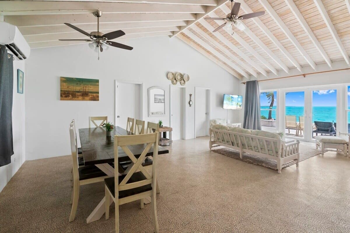 A spacious living area with a dining table, chairs, a sofa, ceiling fans, and a view of the ocean.