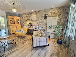 Un salón acogedor con pared de piedra, un mueble de madera, un sillón amarillo, una estructura de cama de metal y una planta en maceta.
