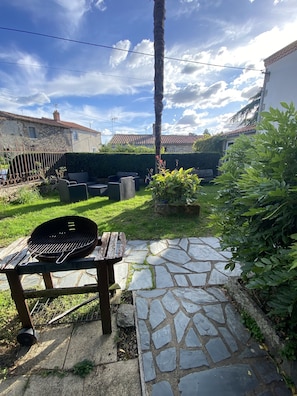 A backyard with a stone pathway, a barbecue grill, outdoor furniture, and a stone wall.