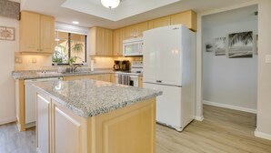 A modern kitchen with granite countertops, wooden cabinets, a white refrigerator, and a microwave. - Covered Lanai & Waterfront View: Cape Coral Condo (Cape Coral)