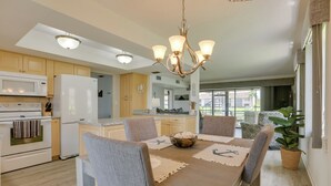 A modern kitchen with a dining area, featuring a chandelier, wooden cabinets, and a large window. - Covered Lanai & Waterfront View: Cape Coral Condo (Cape Coral)