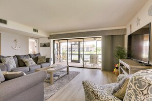 Un salón espacioso con un sofá gris, una mesa de centro y un televisor sobre un mueble de madera.