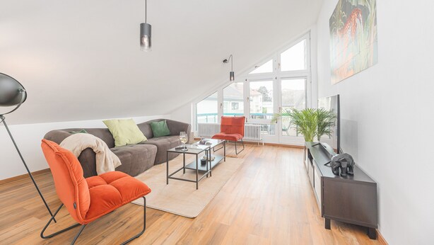 Ein modernes Wohnzimmer mit einer Couch, einem Couchtisch, einem roten Sessel und einem Fernseher auf einem Schrank.