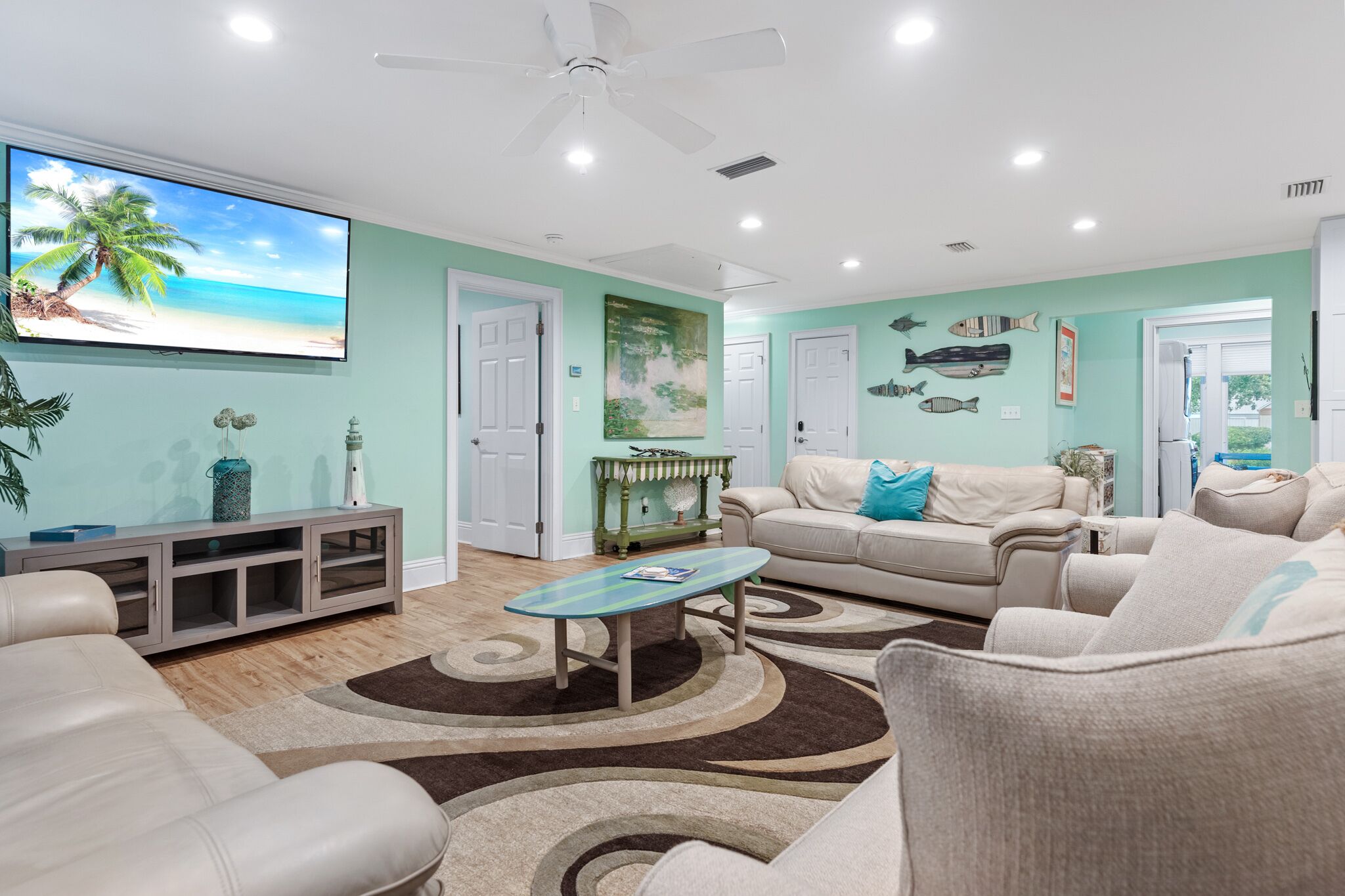 A living room with a flat-screen TV, a ceiling fan, and a large window.