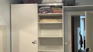 Una habitación con un armario blanco, una mesita con un florero y suelo de madera.