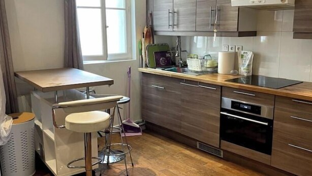 Una cocina moderna con armarios de madera, horno empotrado y una zona de bar con taburetes.