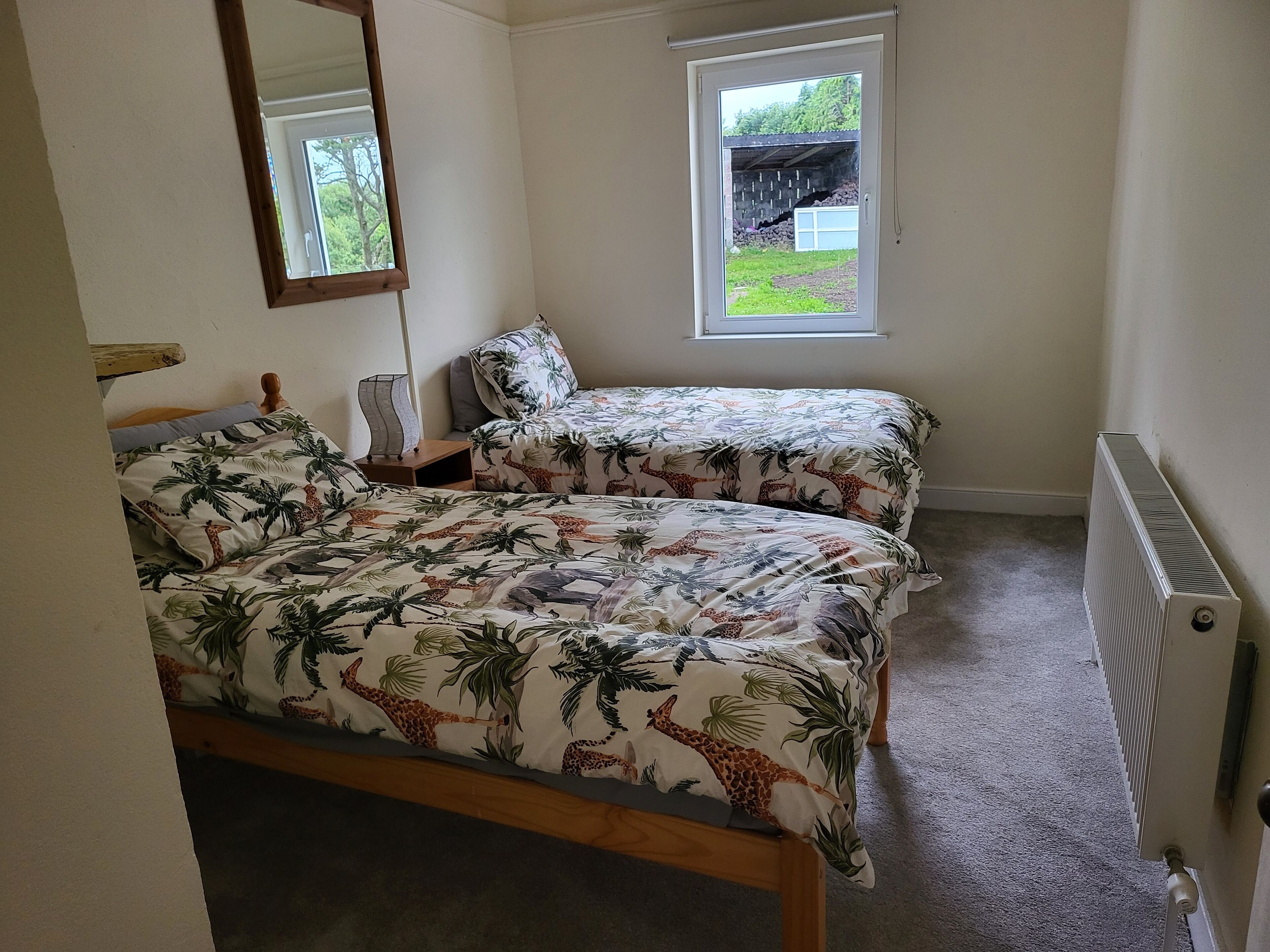 A bedroom with two single beds, a nightstand, a mirror, a window, and a radiator.