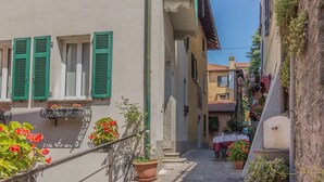 A narrow street with buildings on either side, featuring balconies with potted plants and flowers. - Casa_Greppi_Varenna_varennaholidays (Varenna)
