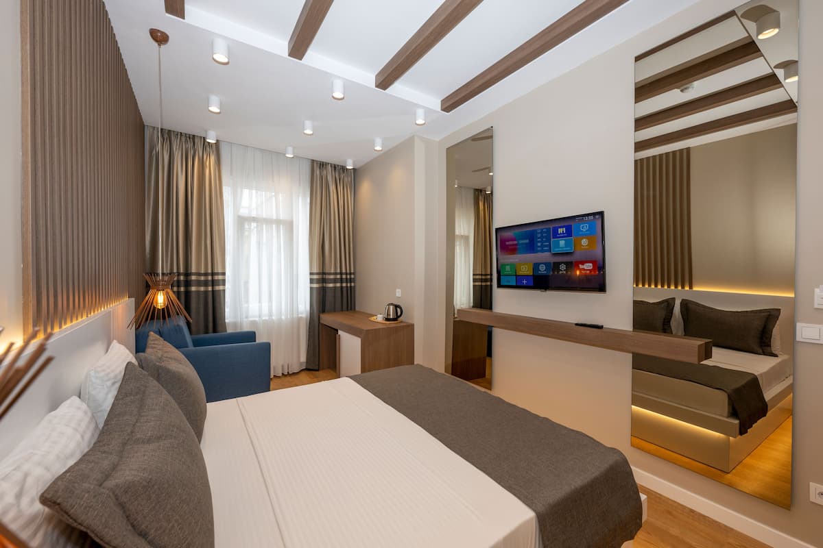 A modern hotel room with a large bed, a desk, a television, and a seating area with curtains.
