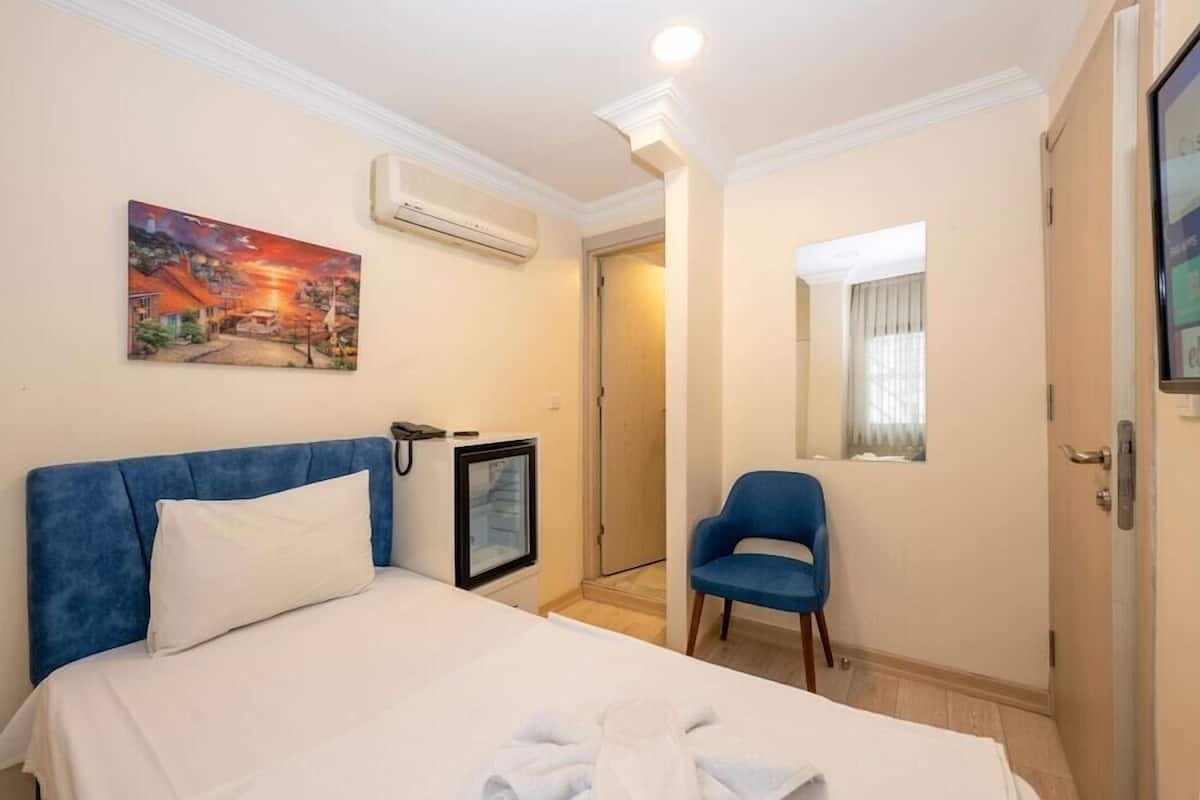 A hotel room with a bed, a chair, a painting, an air conditioner, and a door.