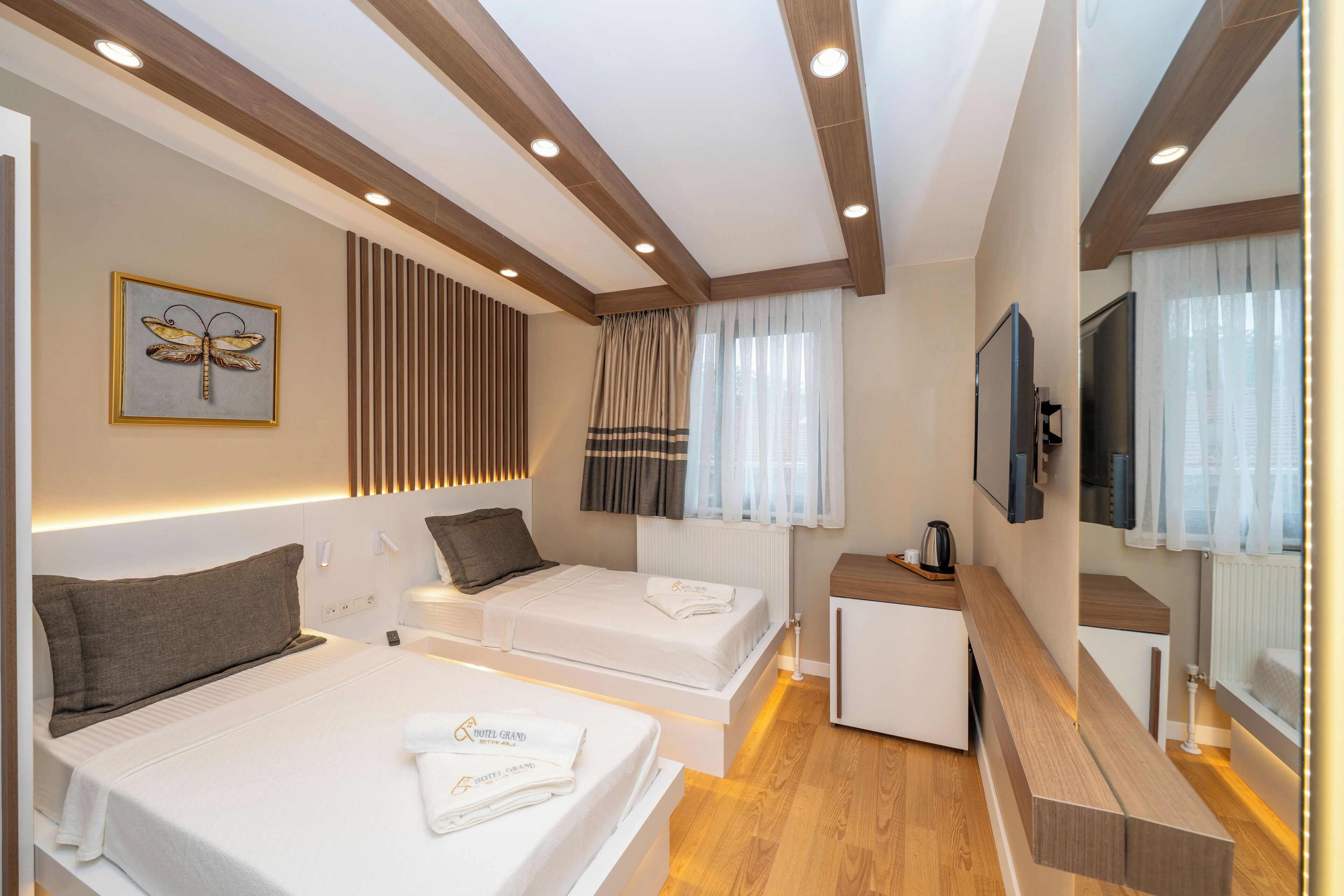 A hotel room with two beds, a TV, a small desk, and a window with curtains.