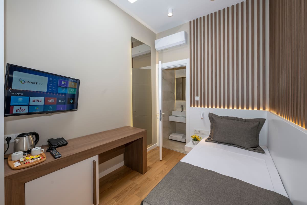 A modern hotel room with a bed, bedside table, and a mounted TV displaying a "Smart TV" interface.