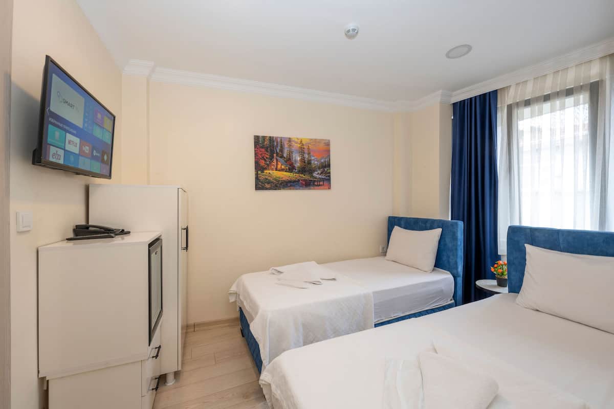 A hotel room with two beds, a TV mounted on the wall, a painting, and a window with curtains.