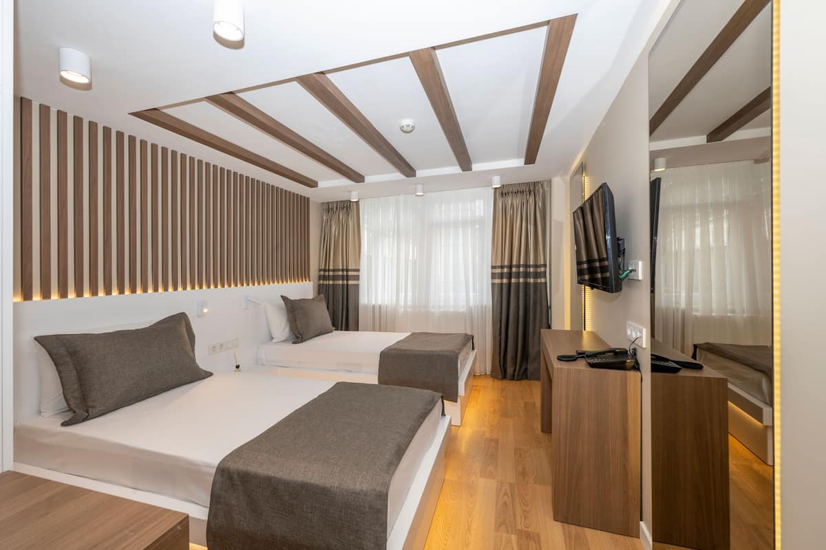 A modern hotel room with two beds, a desk, a TV, and a wooden ceiling.