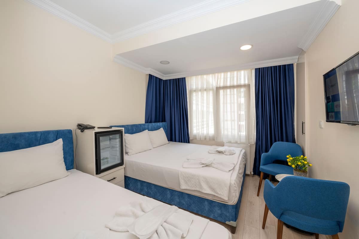 A hotel room with two beds, a TV, a desk, a chair, and a window with curtains.