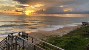 Una pasarela de madera que conduce a una playa con un atardecer de fondo.
