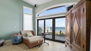 Una habitación con vista a la playa, un sofá de mimbre, un armario de madera y un ventanal grande.