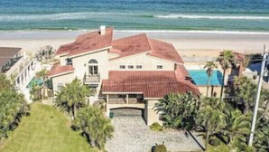 Una propiedad frente a la playa con una casa grande de techo rojo, piscina y vista al océano.