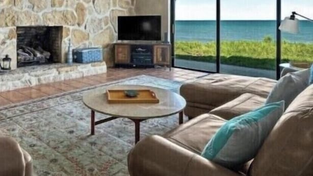 Amplia sala de estar con chimenea de piedra, asientos cómodos y un ventanal con vistas al océano.