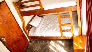A bunk bed with wooden frames and white bedding, a wooden wardrobe, and a window with curtains.