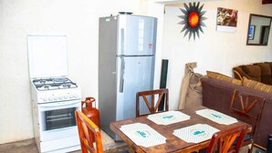 A compact kitchen with a gas stove, a refrigerator, and a dining table with chairs.