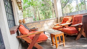 A covered outdoor seating area with wooden furniture and a stone wall.