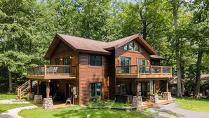 Une cabane en rondins à deux étages, dotée d’un balcon au niveau supérieur, de piliers en pierre et d’un escalier en pierre menant à l’entrée.