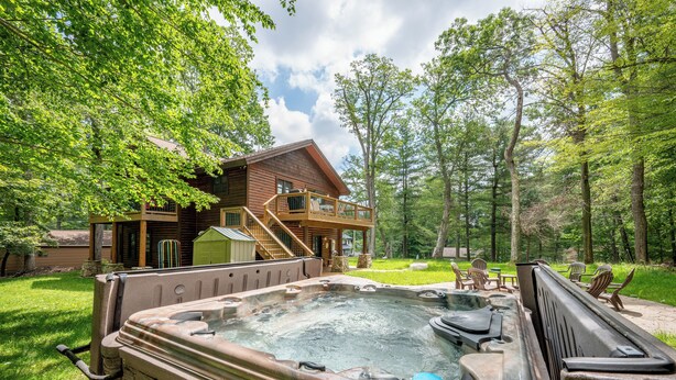 Un bain à remous situé dans un espace boisé, avec un chalet en bois en arrière-plan.