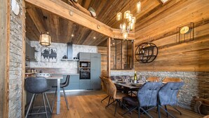 A modern kitchen with a stone wall backsplash, wooden ceiling, and a dining area with bar stools and a round table.