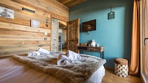 A cozy room with a large bed, wooden walls, a TV, and a small table with a lamp.