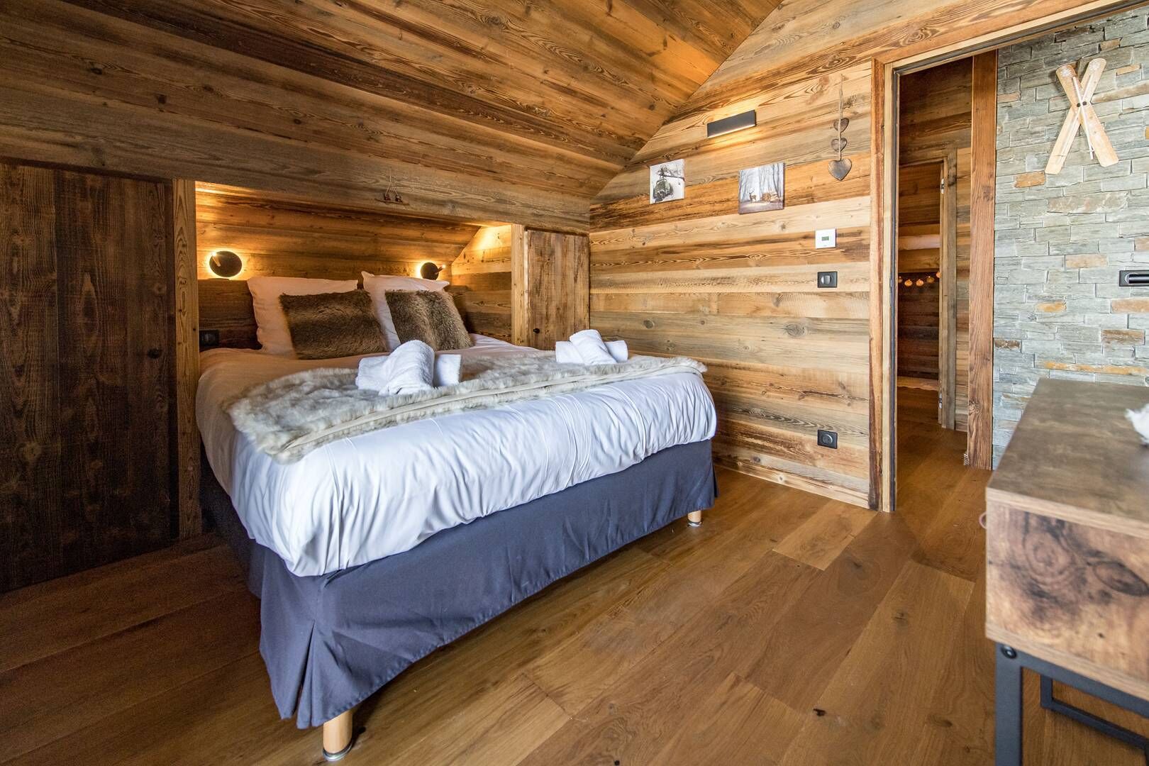 A wooden cabin bedroom with a bed, wooden walls, a stone wall, and a wooden table.