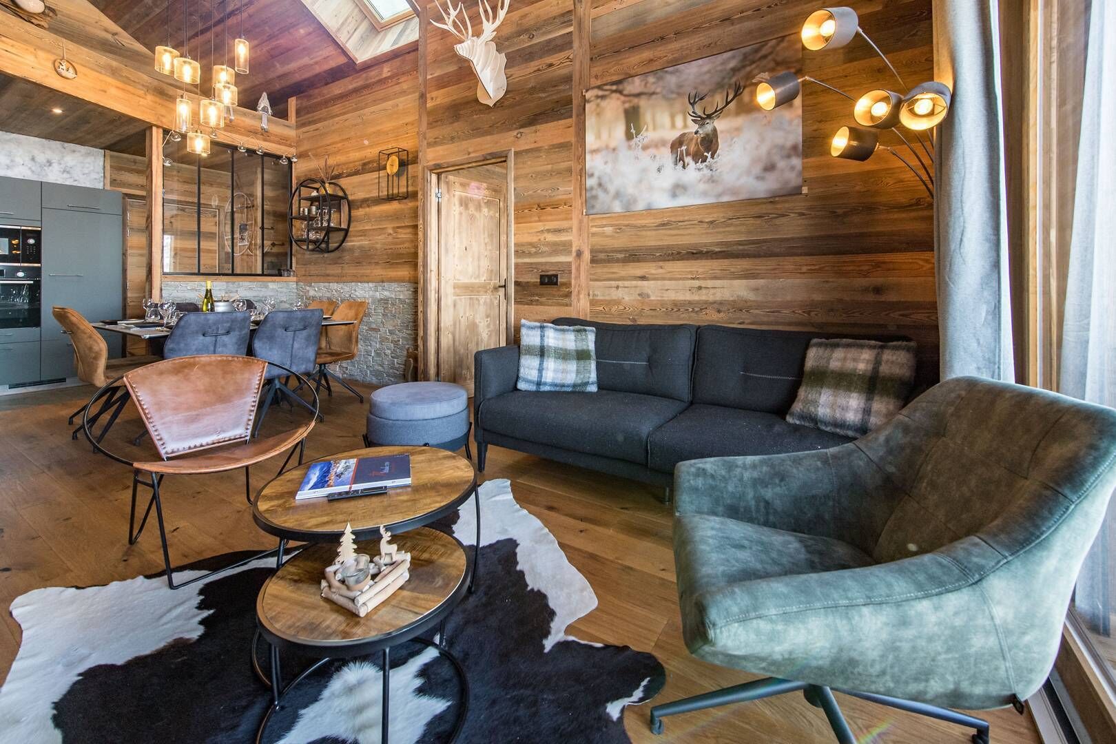 A rustic interior with a wooden wall, a sofa, a leather chair, a dining area, and a kitchen.