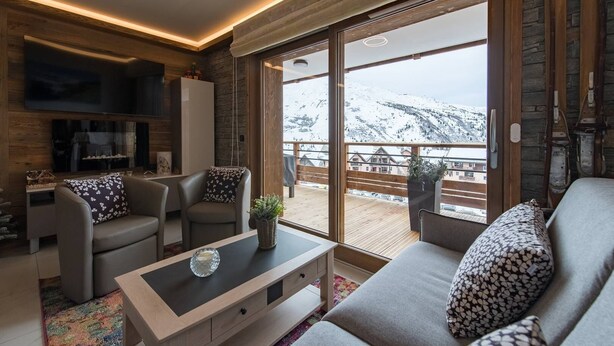 A modern living room with a sofa, armchairs, a coffee table, and a TV. Large windows offer a view of a snowy mountain landscape. - Olvera 402 - New apartment on the slopes (VALMEINIER)