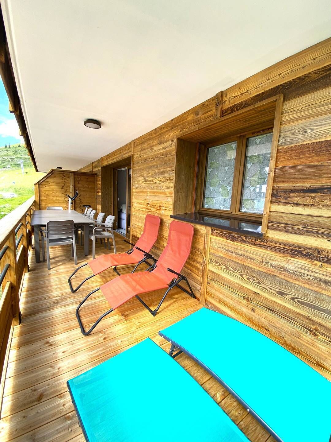 A wooden cabin with a dining area, two red lounge chairs, and a large window.
