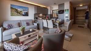 A modern living room with a grey sofa, a coffee table, and a dining area with chairs and a kitchen in the background. - Olvera 402 - New apartment on the slopes (VALMEINIER)