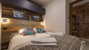 A bedroom with a wooden headboard, a bed with floral and plaid bedding, and a wooden door. - Olvera 402 - New apartment on the slopes (VALMEINIER)